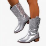 Santiag argentée à talon et broderies élégantes portée par une femme sur fond gris