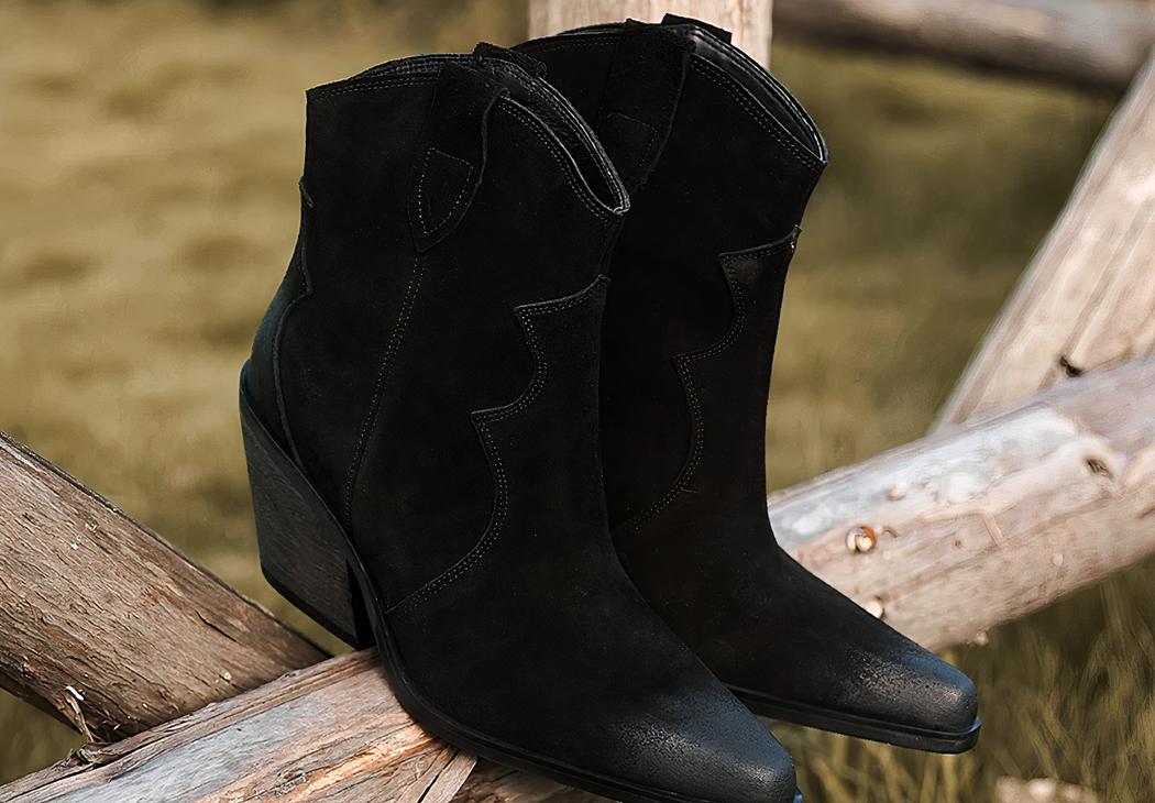 Santiag en daim noir avec talon épais pour femme, sur une rembarde.