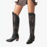 Santiag haute femme en simili cuir noir, porté par une femme, sur un fond gris.