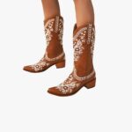 Santiag cowboy marron avec motif floral brodé sur fond gris, portés par une femme